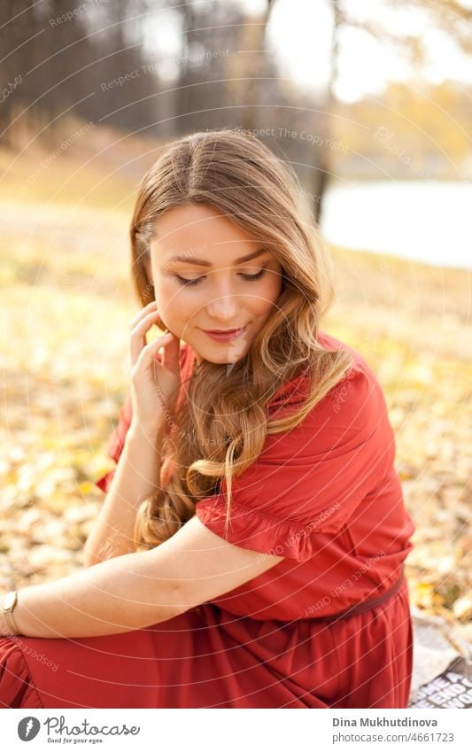 beautiful woman with long in red dresshavingf picnic in the forest by the lake. Romantic picnic in the woods in autumn nature on autumn leaves. adult elegance