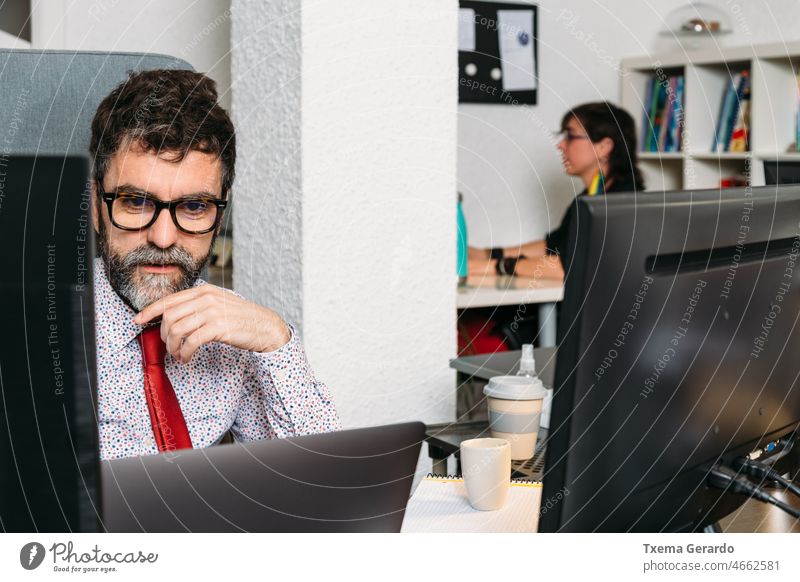 Creative director analyzing the new project created by his team businessman concentration office designer studio beard glasses necktie pc computer desk agency