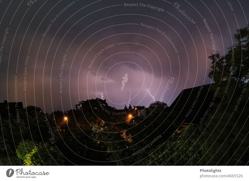 Thunderstorm III ! Lightning in the night sky. In the foreground house roofs and street lamps can be seen. Thunder and lightning Storm clouds Night