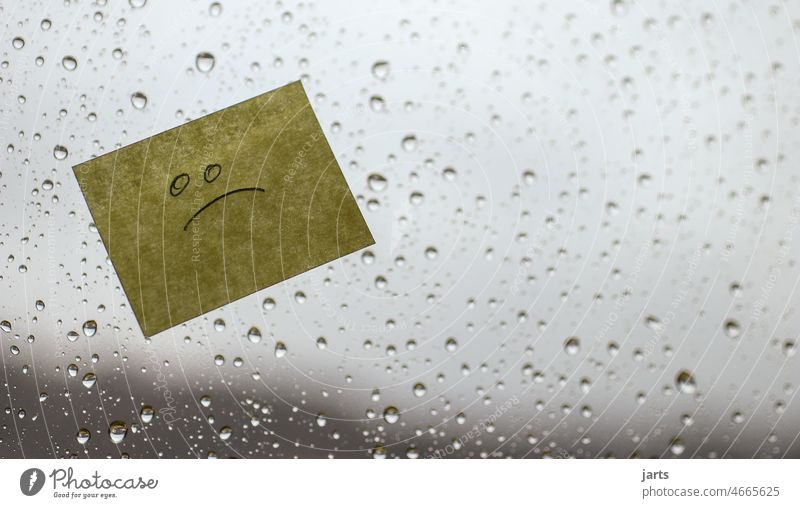 Note with sad face on a rainy window pane, in bad weather. Weather Rain Winter Autumn Gray bleak Bad weather Bad mood Drop raindrops Wet Sky Window Slice