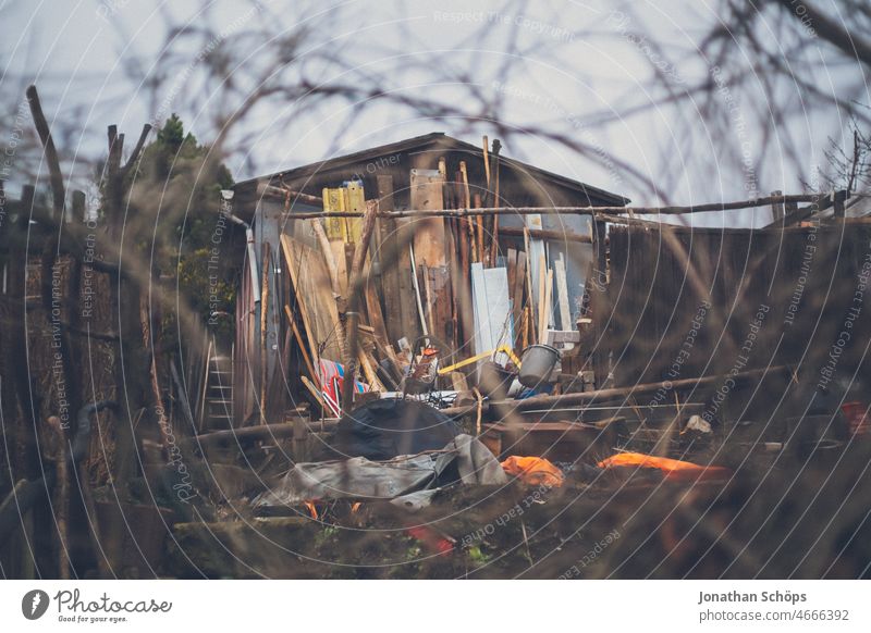 old hut with building material Hut tepid Gardenhouse branches Overview Wood Wooden boards Muddled Deserted Colour photo Exterior shot Nature Bushes