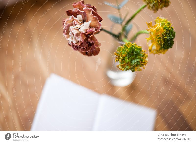 Minimalist flowers in a vase on wooden table and open book - cafe lifestyle background with room for text and copy space. Romantic reading. Floral background with depth of field.