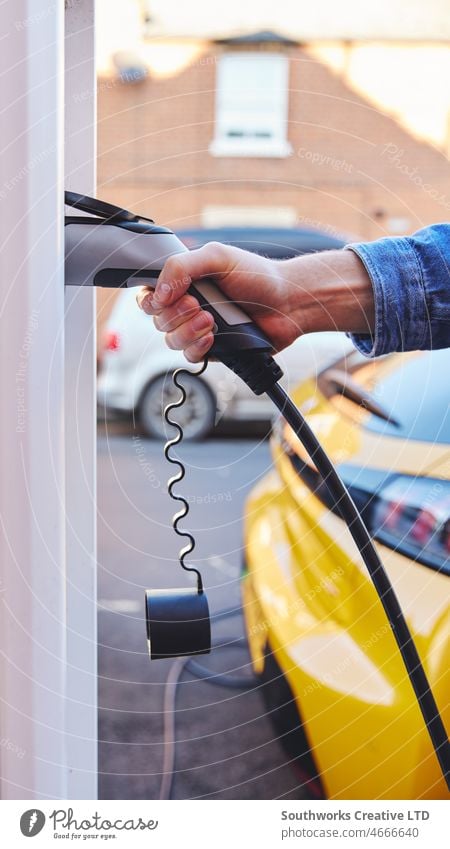 Man plugging in electric car to charging point outside home Electric Car plugged house street road rapid charge vehicle EV station energy battery renewable