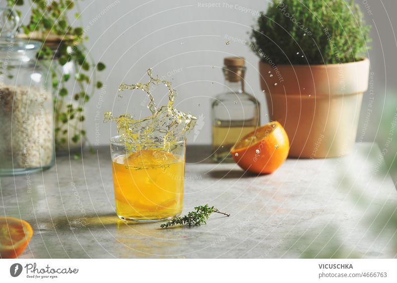 Splash of orange lemonade with herbs at kitchen table splash glass jar bottle halved potted wall refreshing summer drink front view beverage concrete grey home