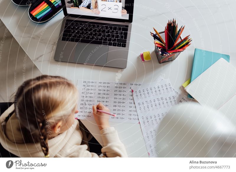 Caucasian kid studying online at home and using laptop. Distance or remote learning for child. Pretty stylish schoolgirl studying homework math during coronavirus covid-19 quarantine and social distancing