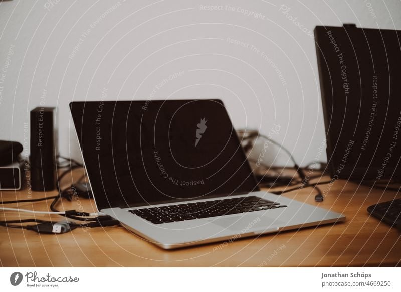 Laptop on wooden table next to external monitor and hard drives with tangled cables Interior shot at home independent Work and employment job Home office