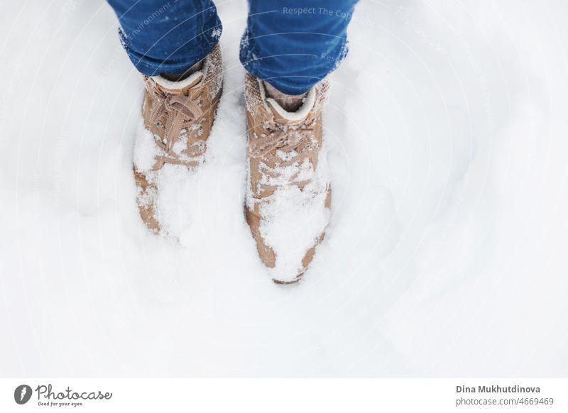 Winter beige shoes or boots in the deep snow in winter park during walk closeup. Woman in jeans and hipster shoes walking in winter forest in the snow. Footwear