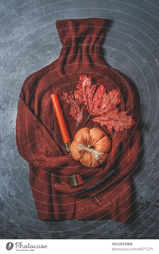 Brown knitted sweater with pumpkin, autumn leaf and orange candle on dark grey background. brown seasonal still life warm clothes fall decoration top view