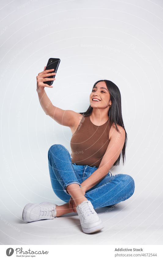 Smiling woman taking photo on smartphone in studio selfie smile self portrait happy social media feminine take photo appearance attire shoot delight female