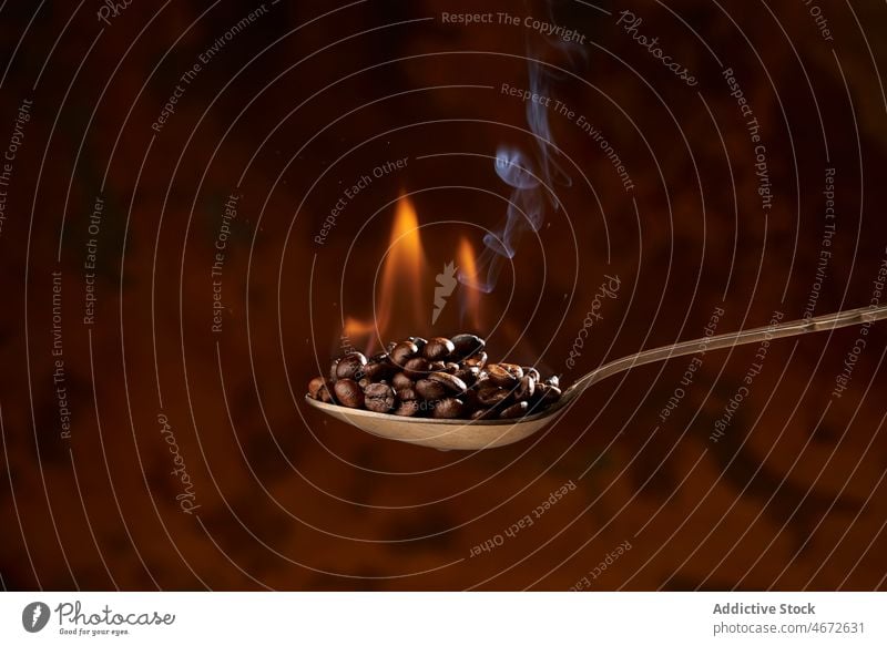 Spoon full of heated coffee beans on brown background roast spoon heap pile fire aroma smoke ingredient energy natural caffeine grain product delicious organic