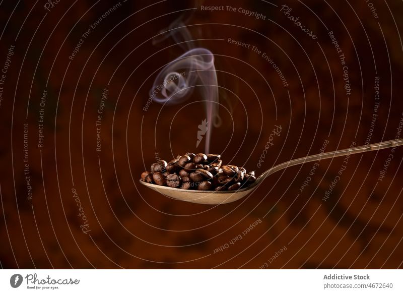 Spoon full of heated coffee beans on brown background roast spoon heap pile aroma smoke ingredient energy natural caffeine grain product delicious organic