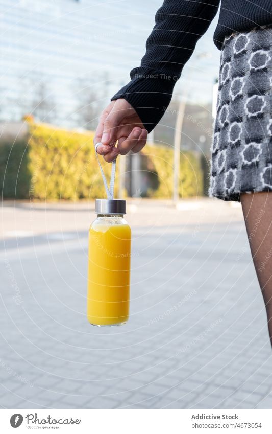 Unrecognizable woman with bottle of juice refreshment beverage street drink city walkway orange female glass lady town vitamin skirt detox sidewalk yummy citrus