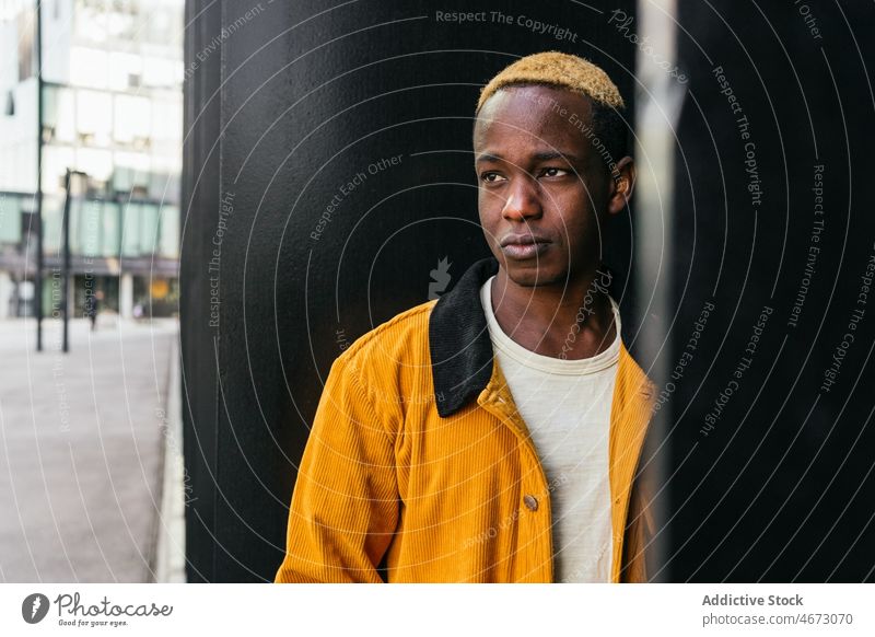 Cool young black man near building style trendy urban street style appearance fashion city dyed hair modern casual short hair wall dreamy pensive confident