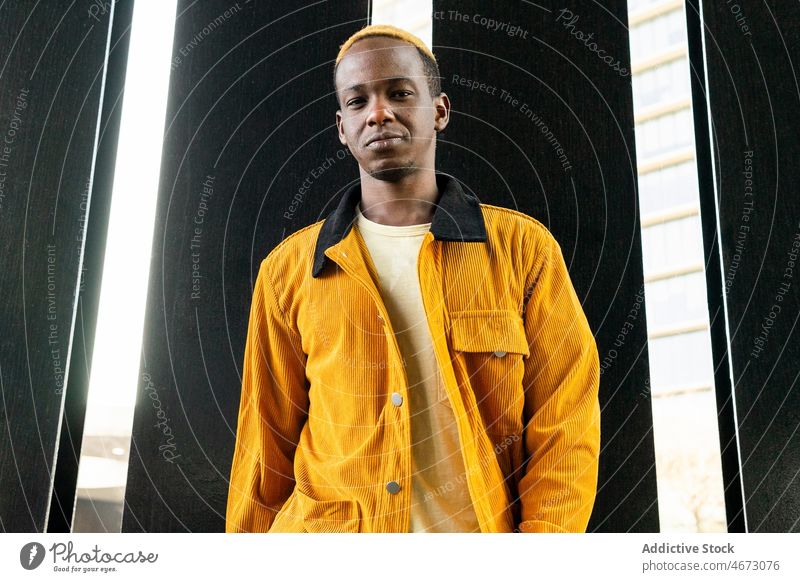 Cool young black man near building style trendy urban street style appearance fashion city dyed hair modern casual short hair wall dreamy pensive confident