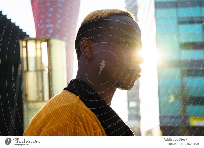 Black man near multistory building style trendy urban street style appearance city dyed hair modern young casual short hair wall dreamy pensive confident