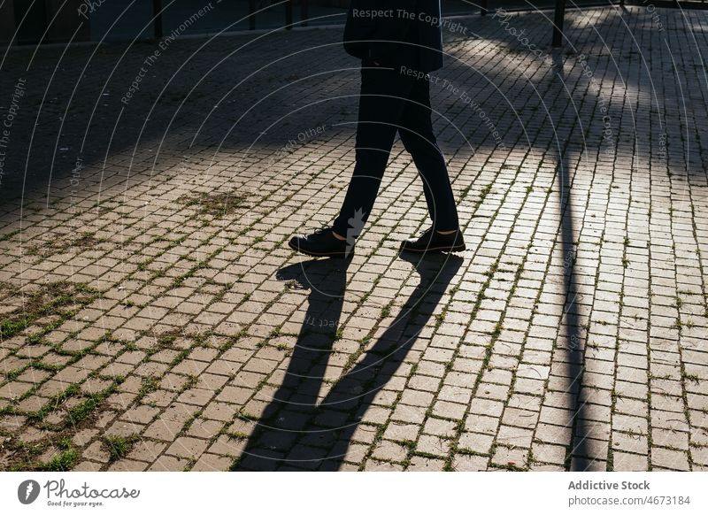 Unrecognizable man walking on pavement street city sunlight walkway sidewalk promenade urban pathway shadow outerwear sunshine town stroll shade bright male