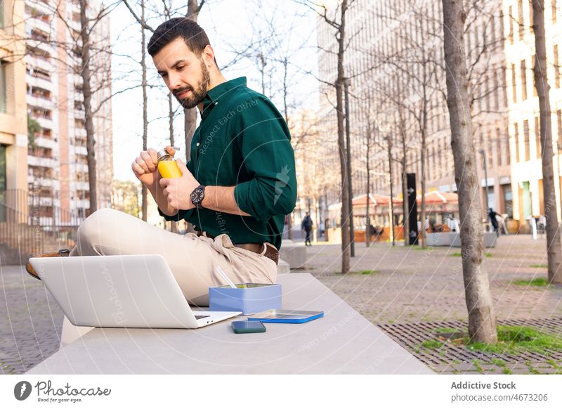 Man with salad browsing laptop on street man entrepreneur typing online work internet lunch meal break food urban remote city modern success businessman male