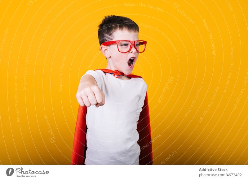 Playful boy in superhero uniform pretending to fly child flight clench fist scream costume portrait studio power kid courage confident cape brave strong