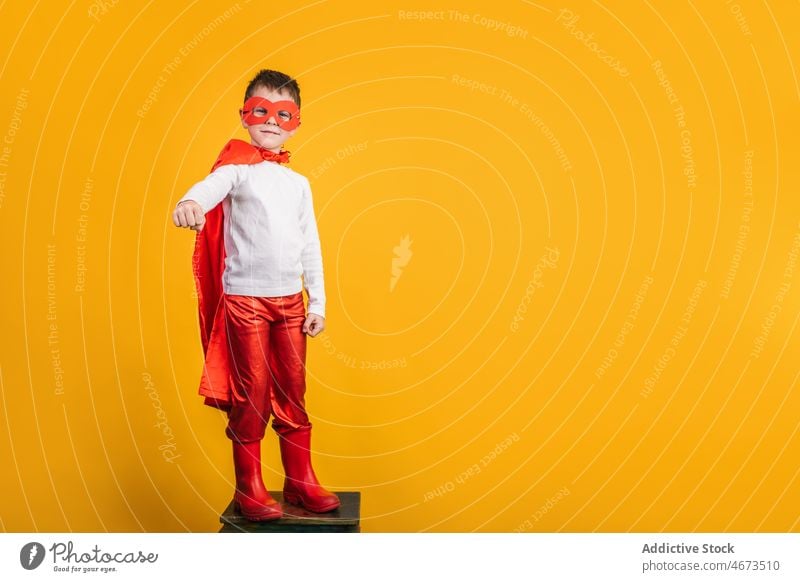 Playful boy in superhero uniform pretending to fly child mask flight clench fist costume portrait studio power kid courage confident cape brave strong