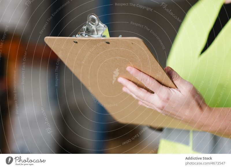 Anonymous woman taking notes while checking supplies warehouse take note write storage work storehouse labourer examine female professional worker focus