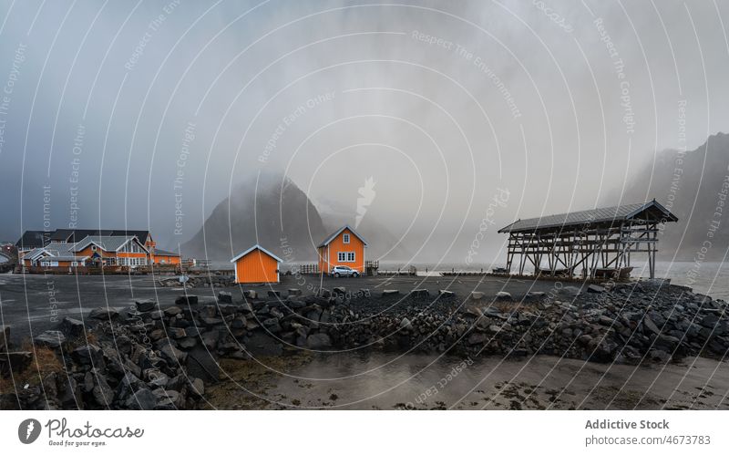 Small coastal village with cottages in bay near snowy mountains settlement sea house shore residential landscape lofoten island norway fjord storm scenic