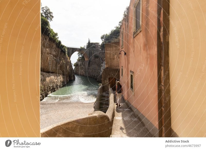 Anonymous woman walking along river and shabby building tourist water rock nature journey trip ancient old aged italy arch stone formation rocky aqua medieval