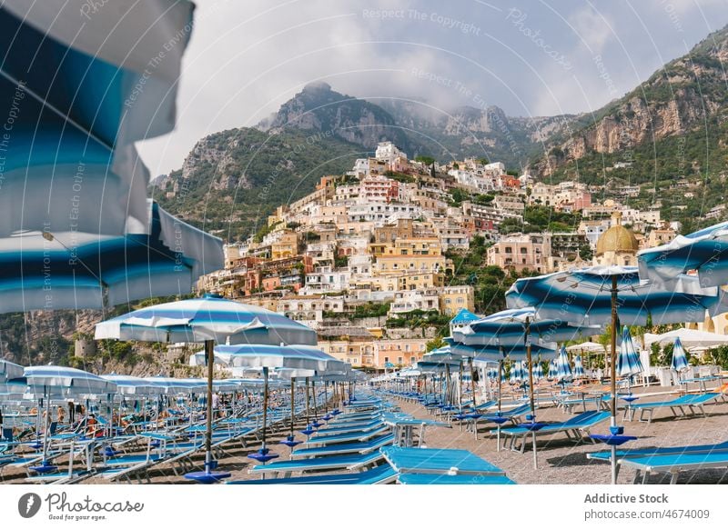 Beach with deckchairs against buildings beach lounge town coast seashore mountain cliff coastal house waterfront umbrella italy environment europe seaside