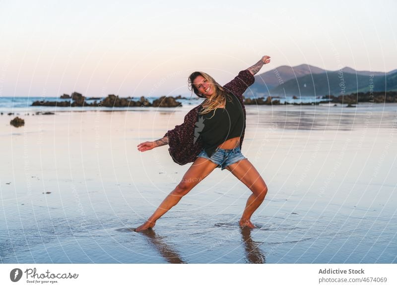 Cheerful woman dancing on wet beach dance water shore coast nature sea recreation activity summer move lady happy female active cheerful positive spread arms