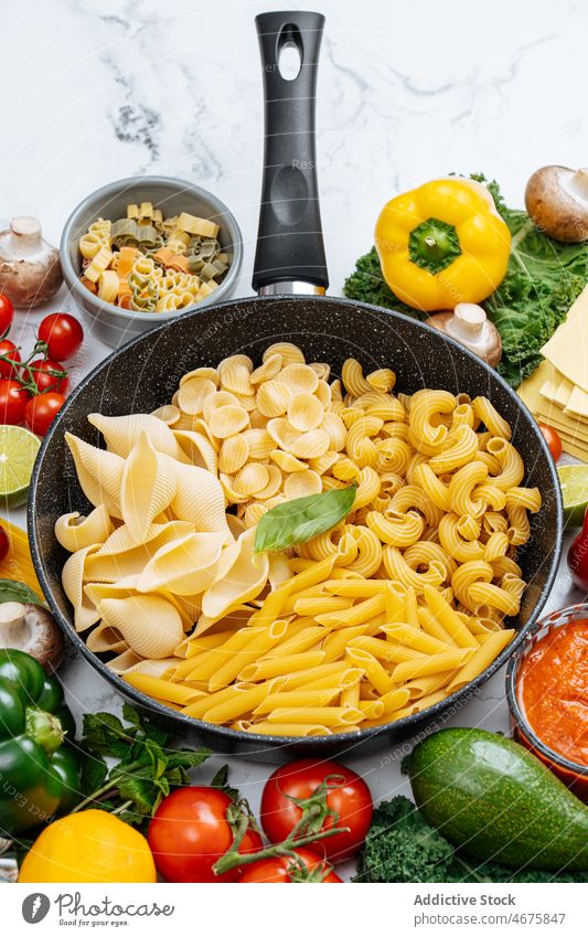 Frying pan with assorted raw pasta amidst vegetables various frying pan uncooked kitchen food recipe culinary cuisine ingredient product prepare bell pepper