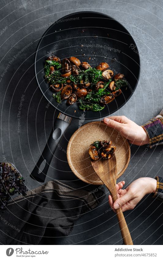 Unrecognizable person serving sauteed mushrooms with greens serve frying pan meal food dish cuisine kitchen table spatula delicious plate tasty culinary