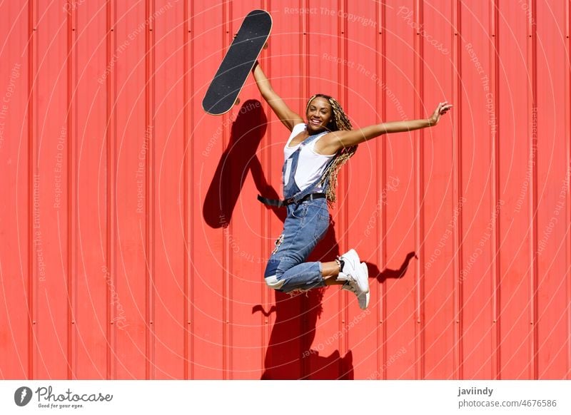 Carefree black woman with skateboard jumping in city skater carefree freedom hipster having fun cheerful summer female ethnic african american afro braids