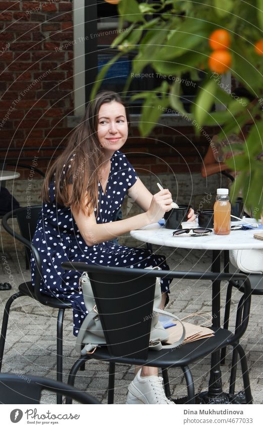 Candid portrait of woman eating at cafe terrace, smiling. Authentic lifestyle of millennial woman in summer in the city. Terrace beautiful relax coffee happy