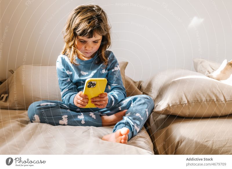 Girl in pajama playing on smartphone girl kid childhood bed bedroom videogame pastime morning domestic apartment adorable barefoot flat cute home female