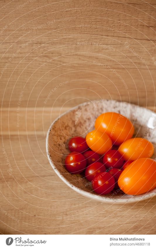 Yellow and red cherry tomatoes in the bowl on wooden table. Organic vegetables for salad. Ripe delicious tomato vertical kitchen background. ingredient style