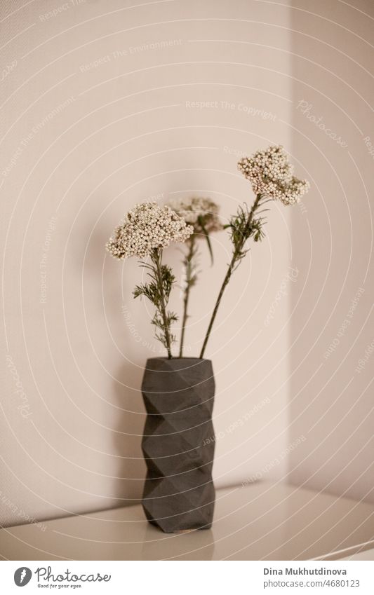 Light and airy photo of three white flowers bouquet in a small vase on coffee table isolated on beige neutral color background. Floral vertical home decor interior backdrop. Romantic surprise.