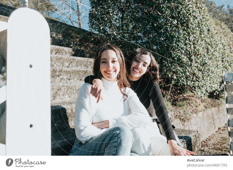 Portrait of a couple of young student woman embracing each other outside the campus resting sitting on stairs and smiling to camera. Happy attitude young and dynamic concept. Trendy and modern style