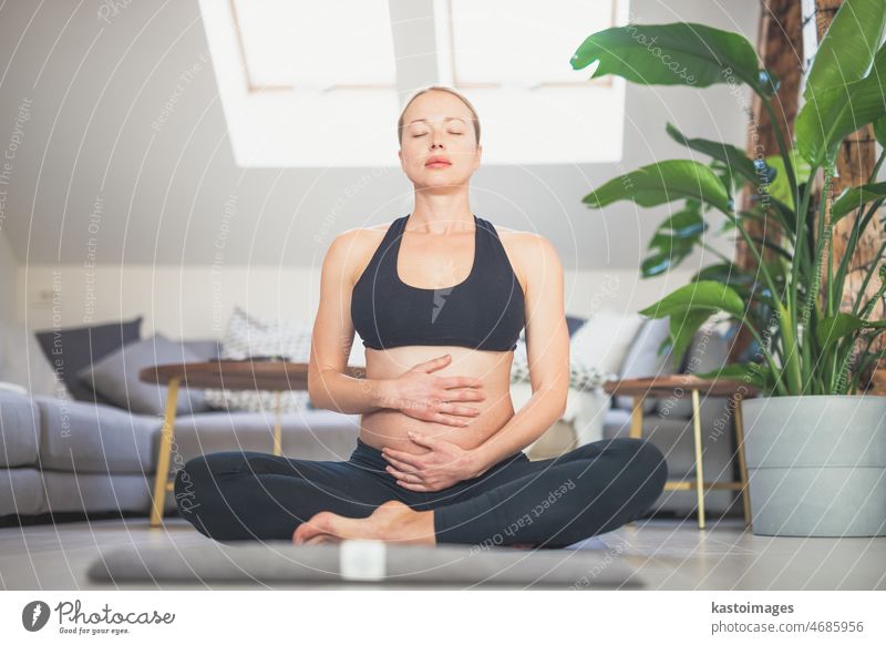 Young beautiful pregnant woman training yoga, caressing her belly. Young happy expectant relaxing, thinking about her baby and enjoying her future life. Motherhood, pregnancy, yoga concept.