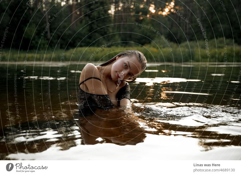 It’s a warm summer’s evening and a gorgeously brunette girl is posing in a river for a pretty portrait. Her clothes are soaking wet but a pretty face is all that matters. The beautiful scenery of wild nature behind her back compliments her wild spirit.