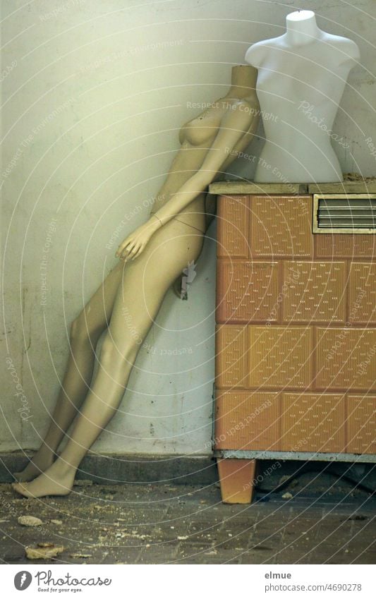 naked, slim, headless, feminine Schaufester doll leans against an old convection oven, on which there is also a torso / giving support Mannequin Naked