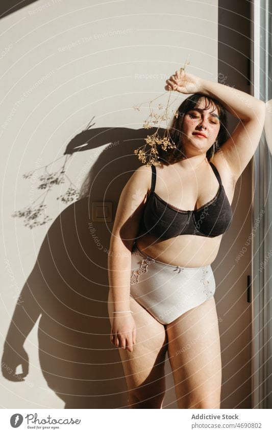 Overweight woman in underwear with dried flowers plus size twig figure sunlight smile lingerie room shadow enjoy feminine makeup windows delight home content