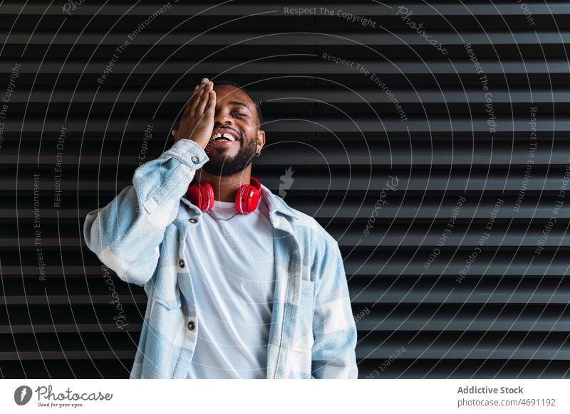 Happy black man with headphones meloman street city wall cover eye smile appearance enjoy african american male happy positive glad content guy style trendy