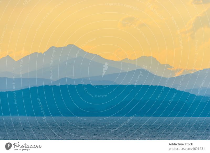 Silhouettes of mountains and sea under cloudy sundown sky landscape sunset seascape silhouette nature scenery scenic dusk picturesque evening sunlight range