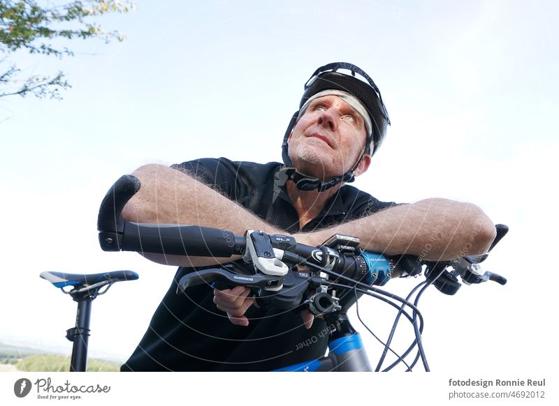 Mountain biker leaning on bicycle handlebars looks into the distance. Moutainbiker Man Bikers Bicycle moutainbike Bicycle handlebars Upper body propped up