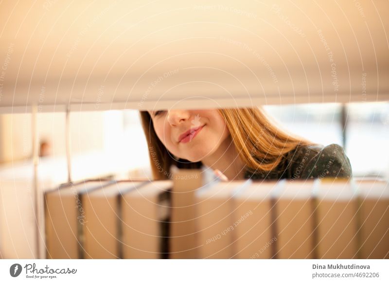 Woman choosing books in bookstore. Young female student picking up a book from a bookshelf at university library. Literature and fiction books. Education and knowledge. Selling and buying books concept. Reading hobby.