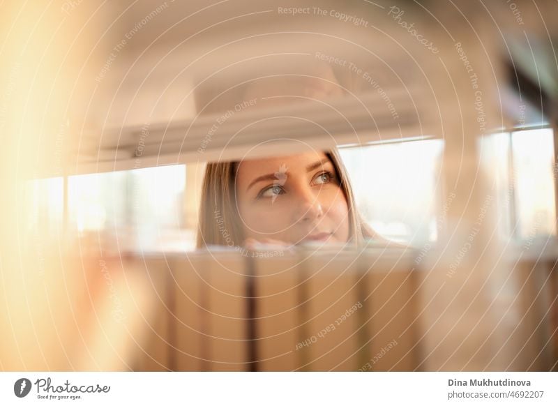 Woman choosing books in bookstore. Young female student picking up a book from a bookshelf at university library. Literature and fiction books. Education and knowledge. Selling and buying books concept. Reading hobby. Face closeup portrait.