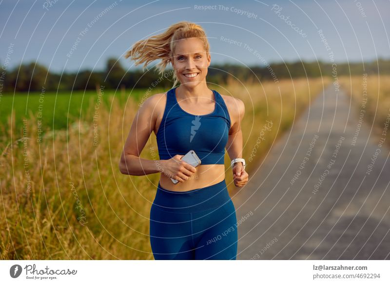 Fit healthy young woman enjoying a jog along a country road passing the camera with a happy smile full of vitality in an active lifestyle concept fit blond