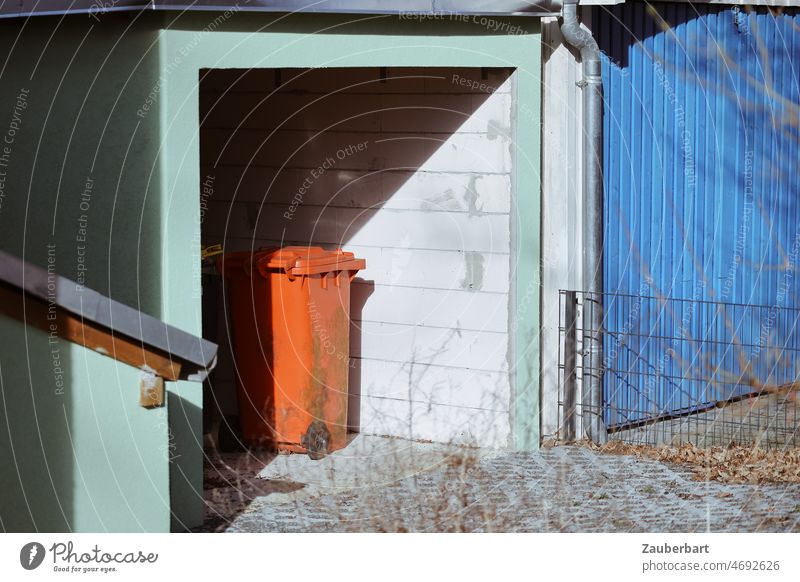 Red garbage can stands in a mint green garage, next to it a blue garage door Trash dustbin Orange waste Garage waste separation Recycling Household garbage