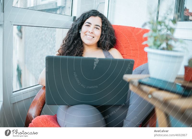 Relaxed plus size curly young woman smiling to camera while using a laptop to prepare,post and do training online. Training clothes. Getting fit for the summer concept. Beach body preparation