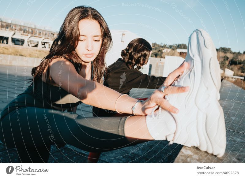 Two woman stretching leg before starting running jogging outdoors on urban place. Training losing weight with friends together smiling to camera happy. African arab people doing exercise.