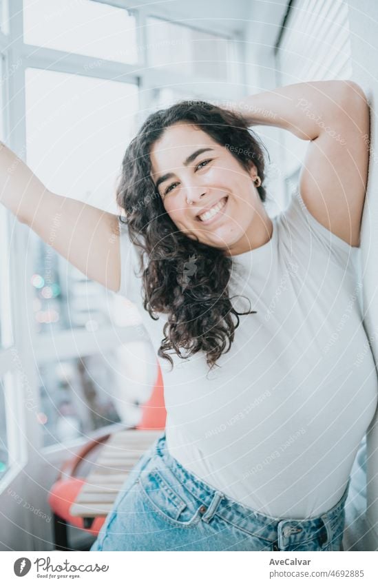 Curvy young woman smiling to camera while dancing and celebrating success at home, accomplishing challenges. Modern city flat. Working on targets and mental health concerns. Close up portrait